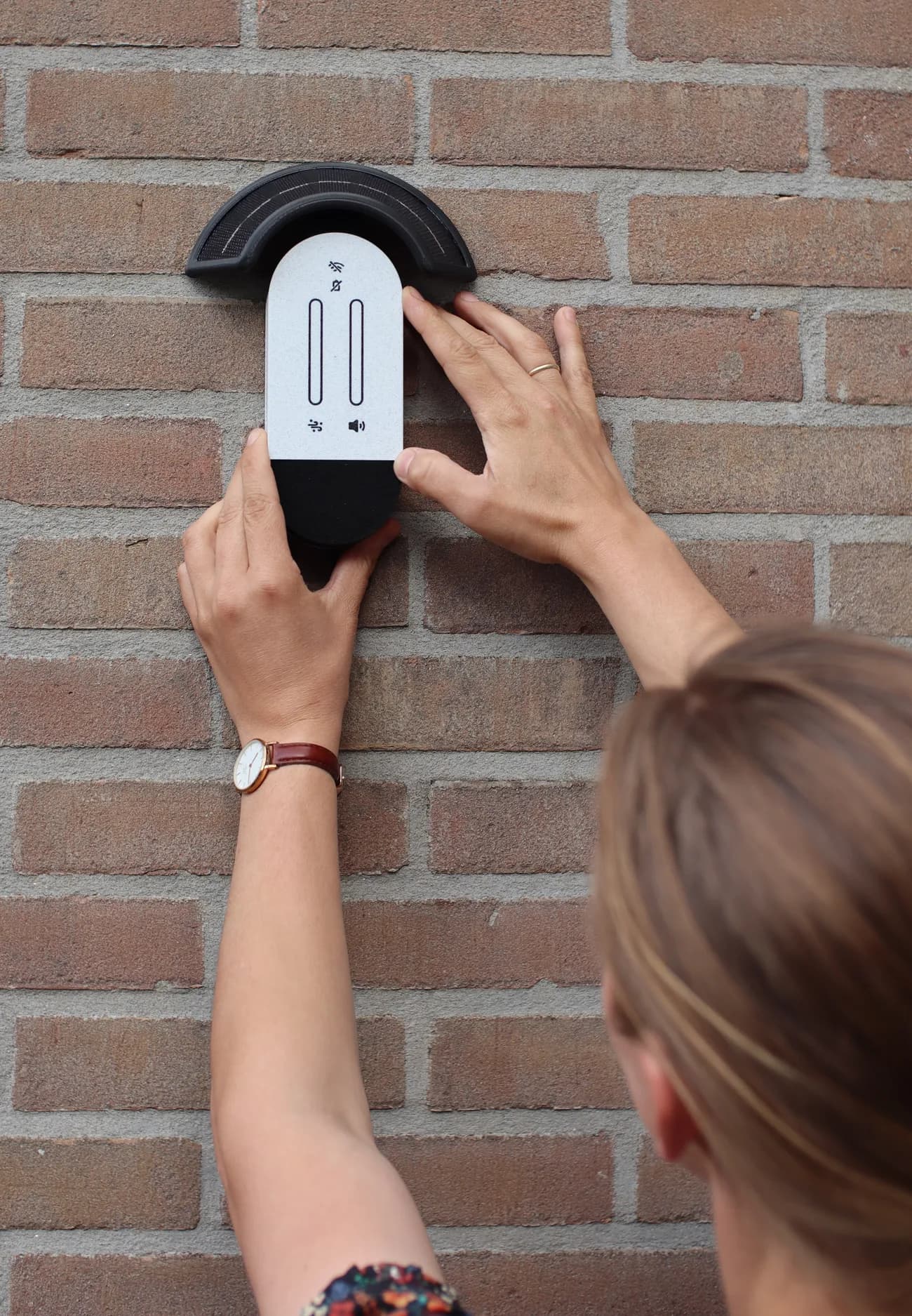 Een bewoner hangt een MedeMeter aan een buitenmuur